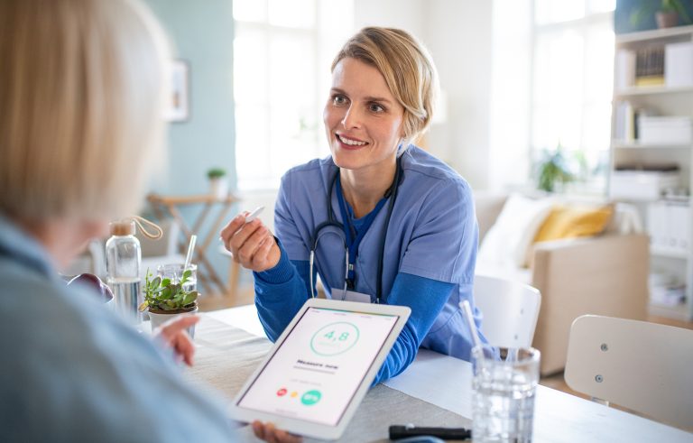 Senior Woman With Caregiver Or Healthcare Worker Indoors, Using Tablet.